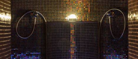 Un baño con paredes de mosaicos y dos lavamanos de metal.