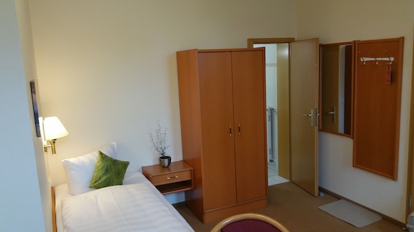 Una habitación de hotel con una cama, un armario de madera, una mesita de noche con lámpara y un espejo en la pared.