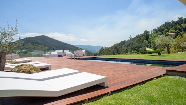 A modern outdoor deck with lounge chairs and a swimming pool, surrounded by lush greenery and hills. - Quinta do Bosque (Baiao)