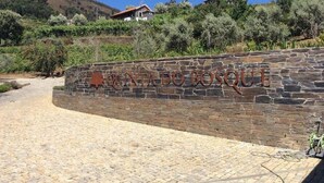 A stone wall with the inscription "QUINTA DO BOSQUE" and a vineyard in the background. - Quinta do Bosque (Baiao)