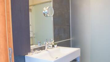 Un baño moderno con un espejo grande, lavamanos blanco y paredes cubiertas de azulejos oscuros.