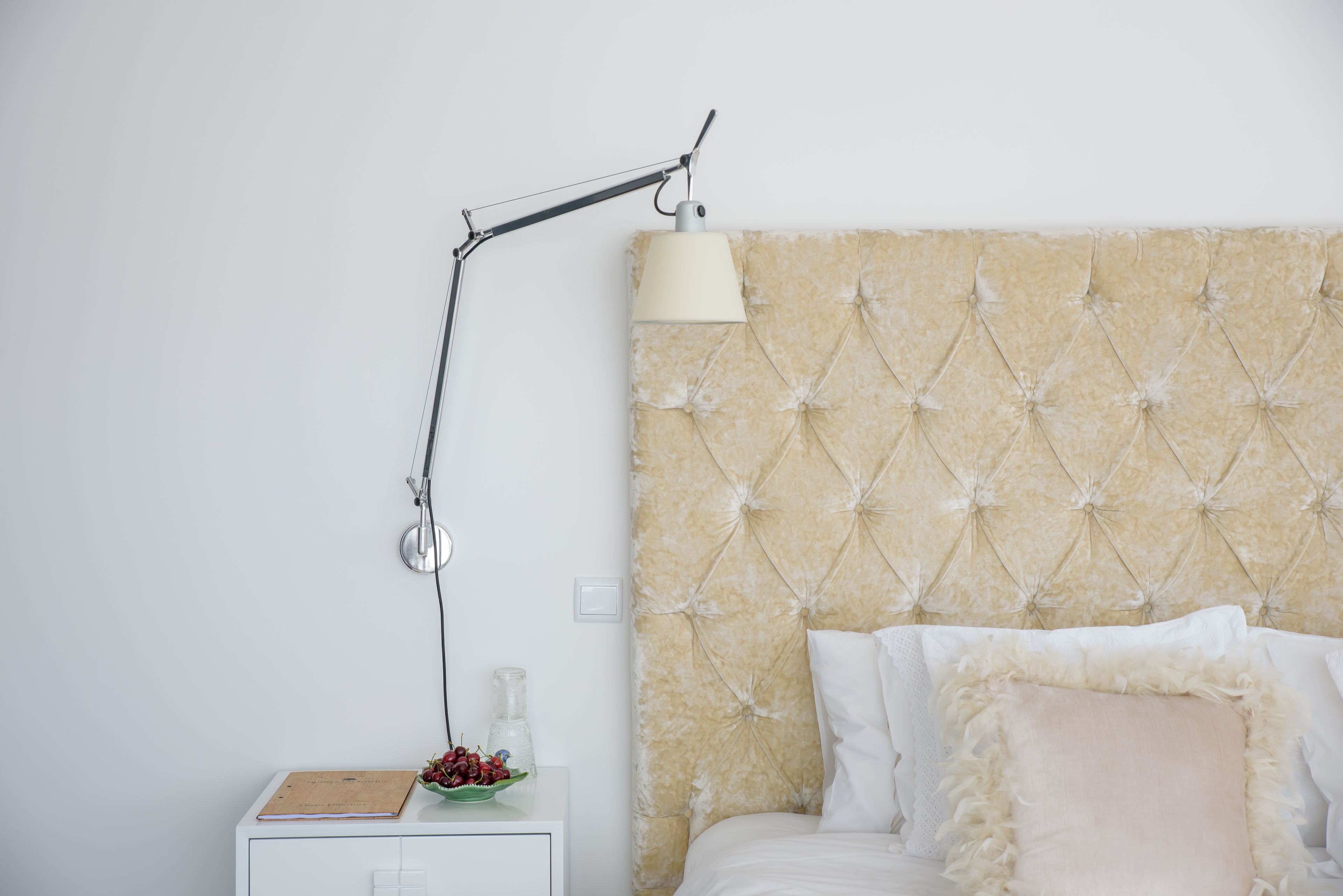 A neatly arranged bedroom with a tufted headboard, a bedside table with a lamp, and a small plant.