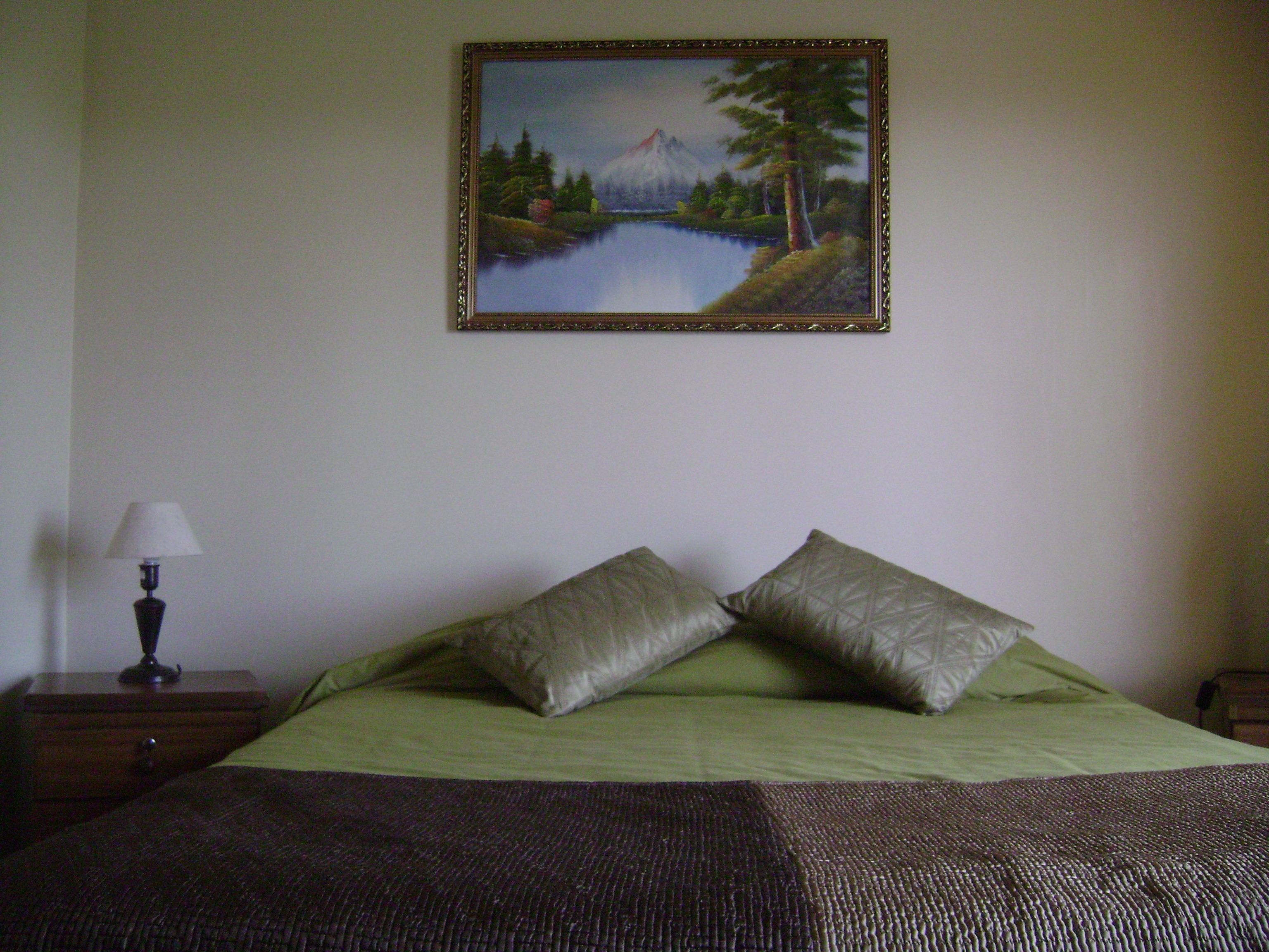 A bedroom with a bed, pillows, a nightstand, and a lamp.