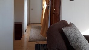 A hallway with a wooden floor, a brown sofa, and a door with a curtain. - Cabañas Lago Azul (Puerto Varas)
