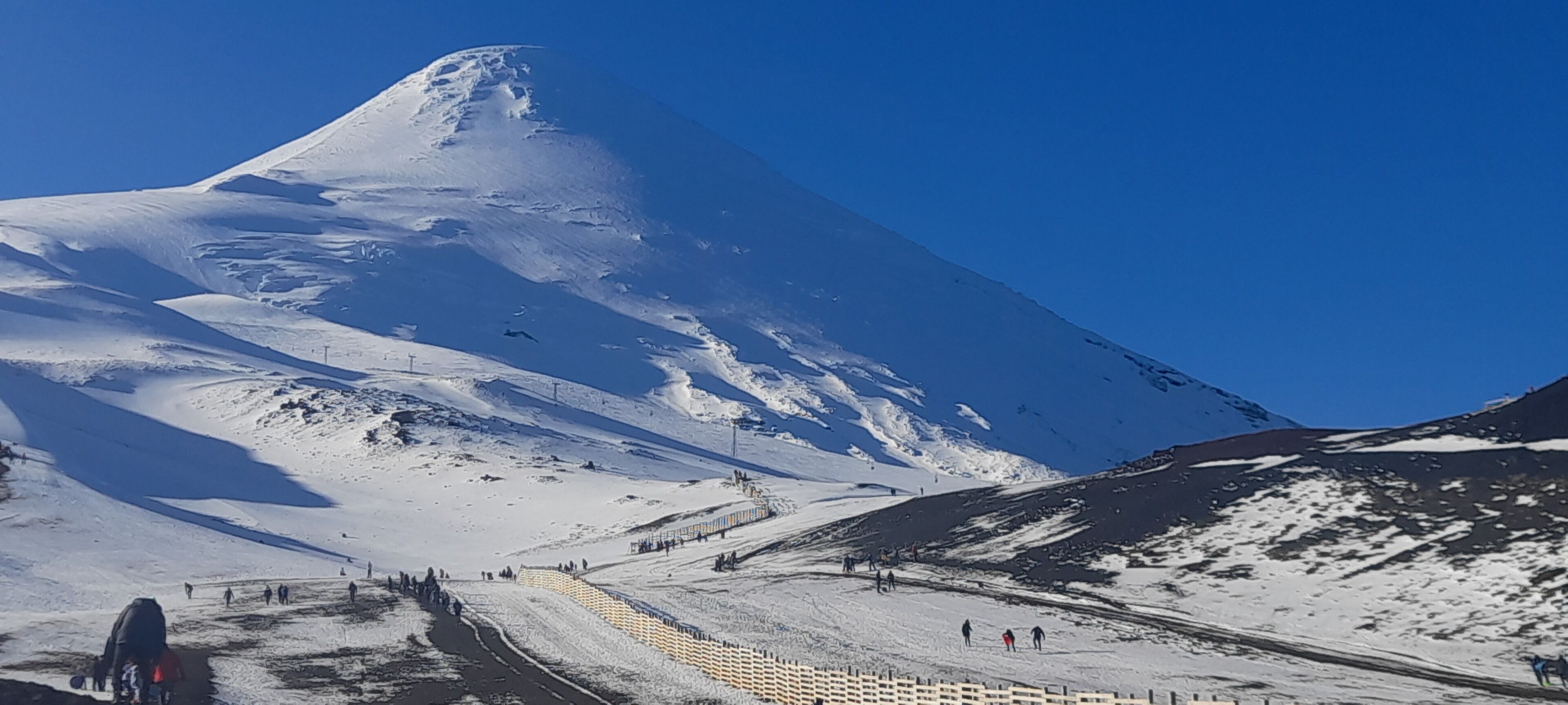 A snow-covered mountain with a ski slope and a fence.