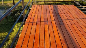 A wooden deck with a metal railing overlooking a green field and a distant view of the sea. - Cabañas Lago Azul (Puerto Varas)