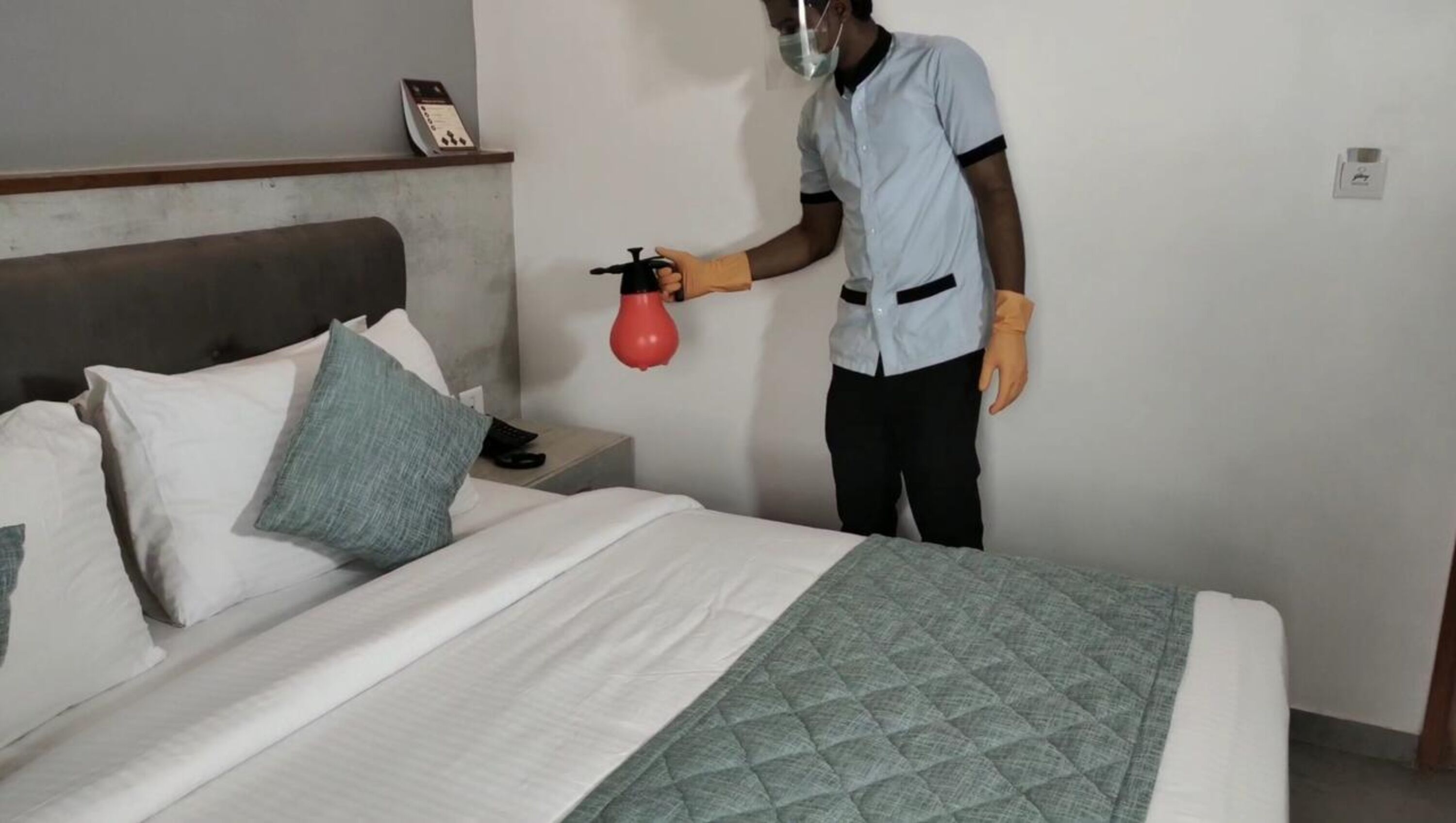 A hotel room with a bed, pillows, a nightstand, a phone, and a red spray bottle.