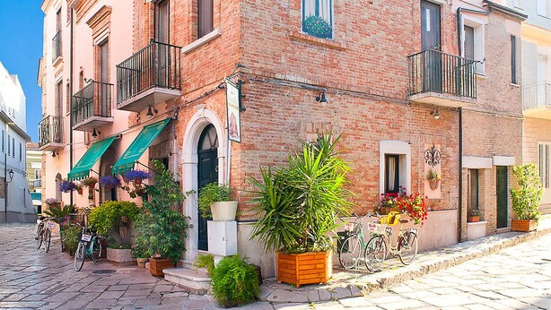 Un bâtiment traditionnel en briques, doté de balcons, situé sur une rue pavée et agrémenté de plantes en pot.