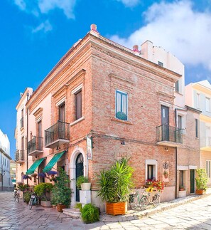 Un bâtiment traditionnel en briques, doté de balcons, situé sur une rue pavée et agrémenté de plantes en pot.