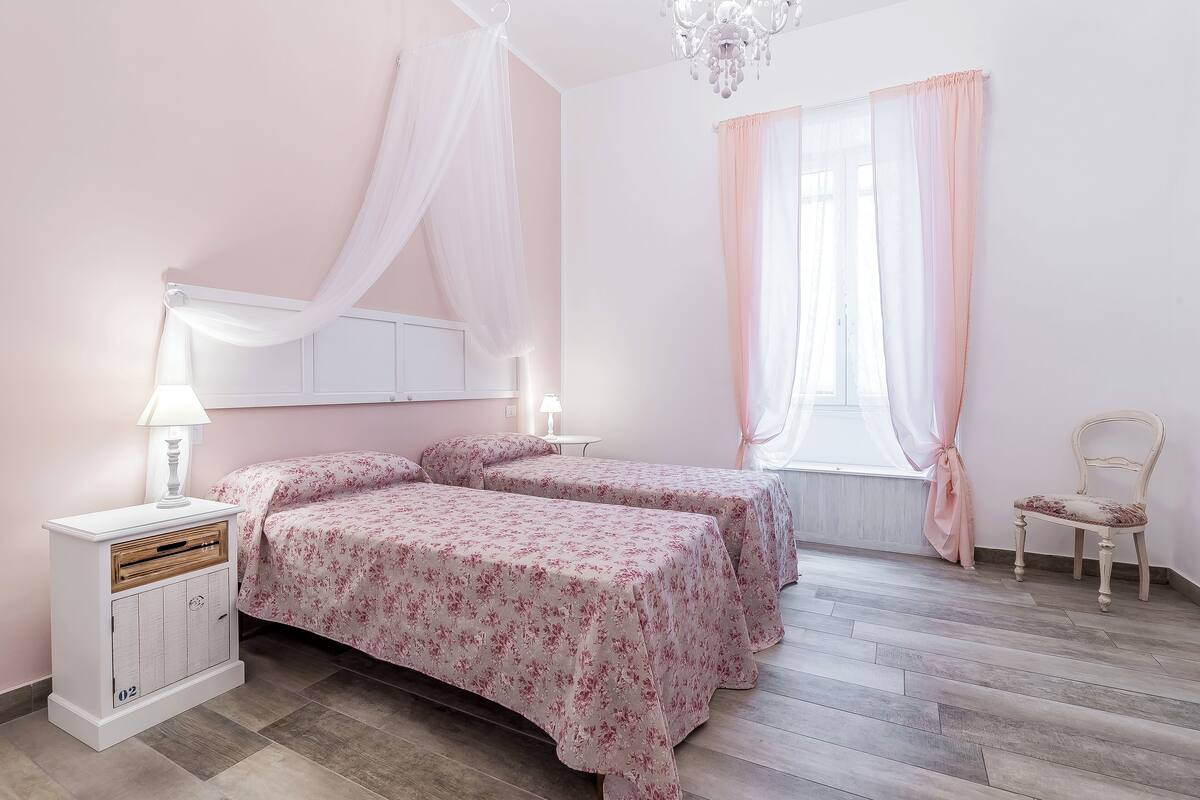 Un dormitorio con dos camas, una mesita de noche, una silla y una ventana con cortinas.