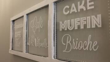 Un mur orné de trois panneaux encadrés, chacun indiquant un type de pâtisserie différent : « GÂTEAU, MUFFIN, BRIOCHE ».