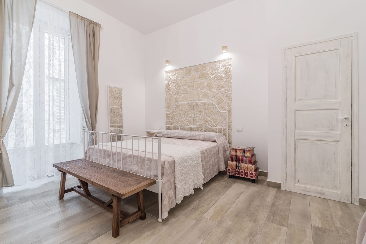 Un dormitorio con cama, un banco, un armario y un adornado en la pared.