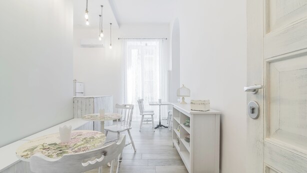 A bright, white interior with a dining area featuring a table and chairs, a kitchen area with a counter and shelves, and a door with a lock. - Le Villanelle B&B (Naples)