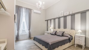 A bedroom with a large bed, bedside tables, a chandelier, and a window with curtains. - Le Villanelle B&B (Naples)