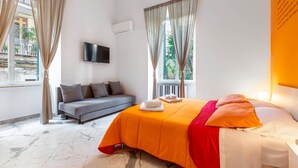A hotel room with a bed, a sofa, a flat-screen TV, and a window with curtains. - B&B Colori e Note (Naples)