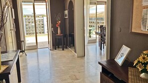 A spacious living area with a view of the outside, a dining area with a table and chairs, and a reception desk with a vase of flowers.