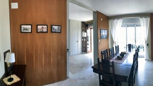 A dining area with a long table and chairs, a lamp, and framed pictures on the wall.