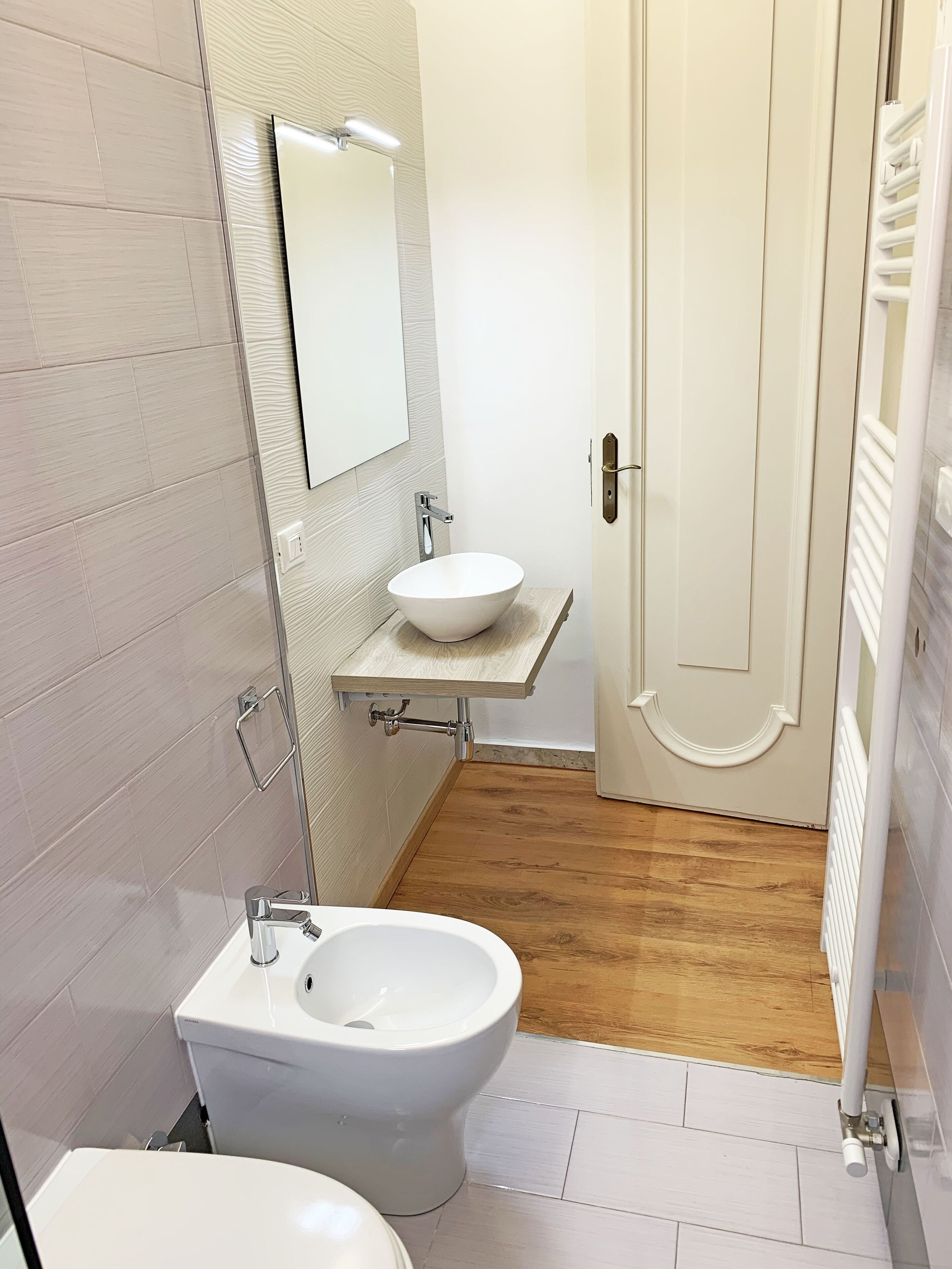 A bathroom with a white toilet, a white bidet, a white sink on a wooden countertop, and a mirror above the sink.
