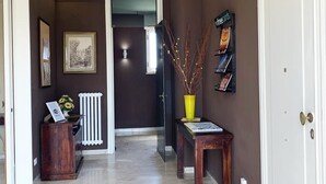A hallway with a marble floor, a radiator, a framed picture, a small table with a vase, and a door with a brass handle.