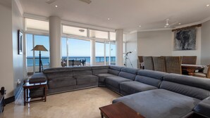 A spacious living area with a large gray sectional sofa, a wooden coffee table, and a view of the ocean through large windows. - 702 Oyster Rock (Umhlanga)