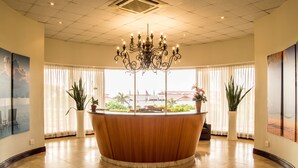 A reception area with a wooden reception desk, large windows with sheer curtains, potted plants, and a chandelier. - 702 Oyster Rock (Umhlanga)