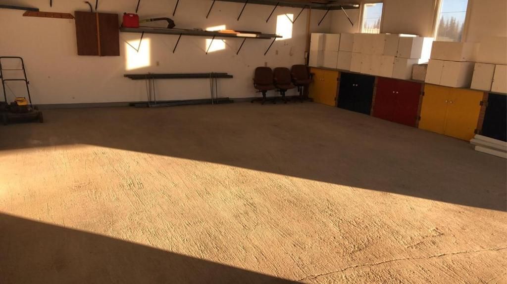 A spacious indoor area with a concrete floor, a bench, and chairs along the wall.