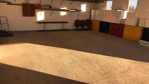 A spacious indoor area with a concrete floor, a bench, and chairs along the wall. - Moose Motel (Smooth Rock Falls)