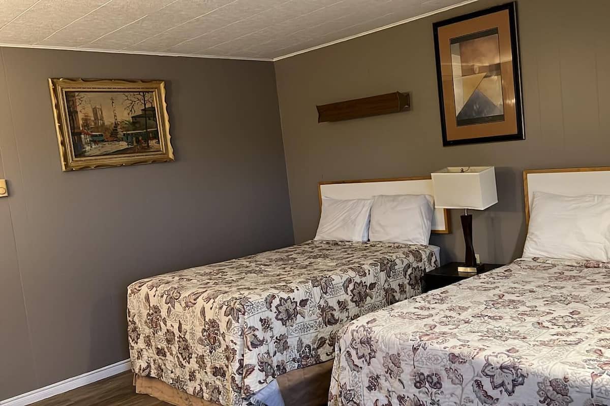 Quarto de hotel com duas camas, colchas estampadas com flores, um quadro na parede e uma mesa de cabeceira com abajur.