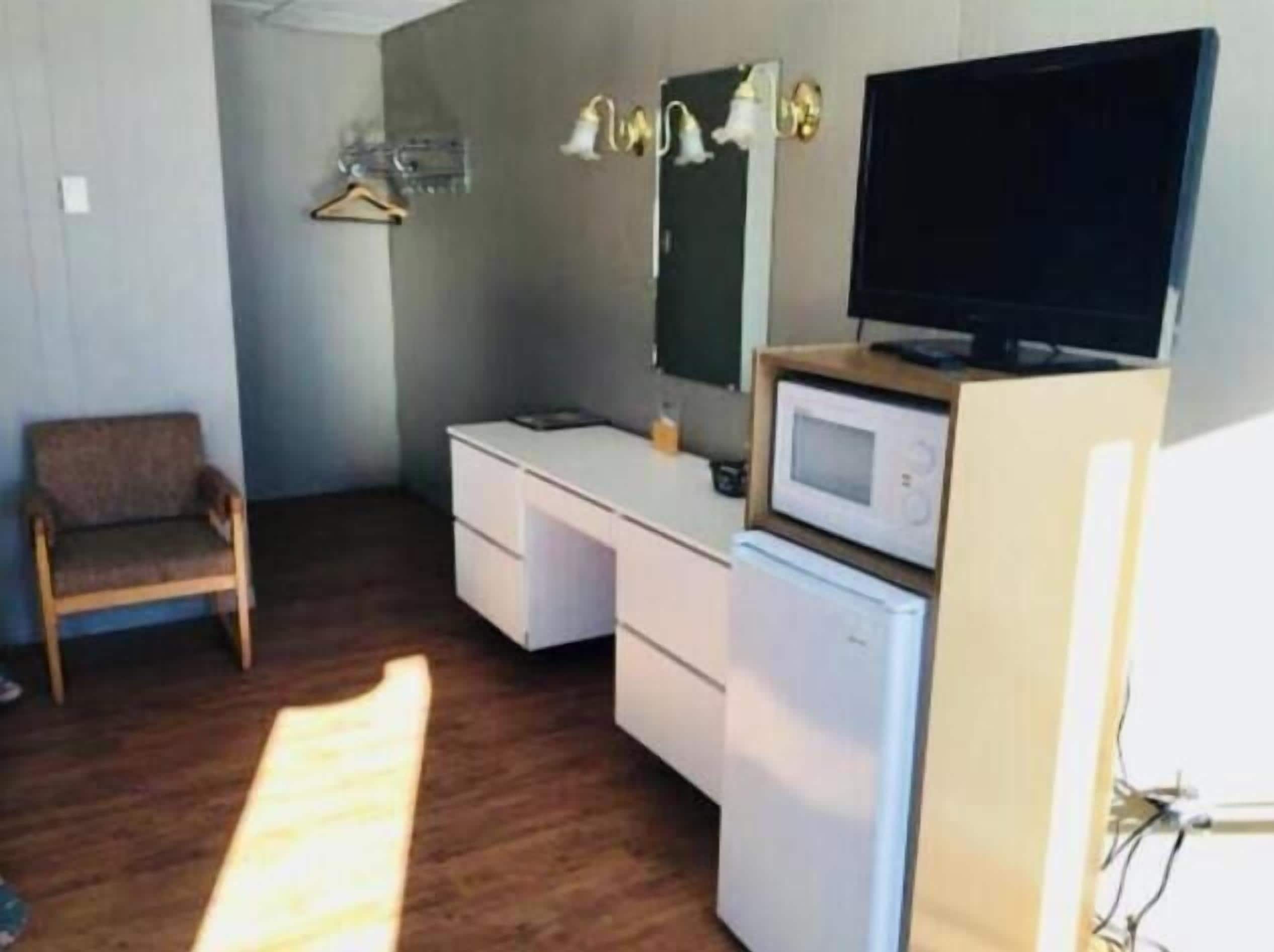 A room with a white desk, a chair, a television on a stand, a microwave, and a small refrigerator.