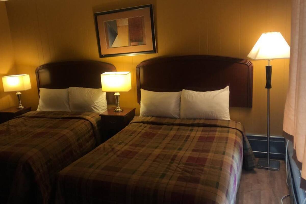 Quarto de hotel com duas camas, cada uma com cabeceira e mesa de cabeceira com abajur.