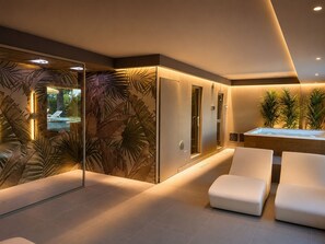 A modern spa room with a glass-enclosed sauna, a hot tub, and white cushioned seating. - Hotel Residence Turium (Santa Maria del Cedro)
