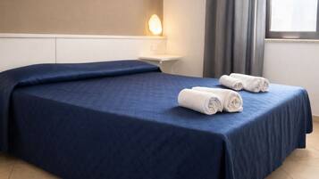 Una camera d'albergo con un letto grande, un comodino, una lampada a parete e una finestra con tende.