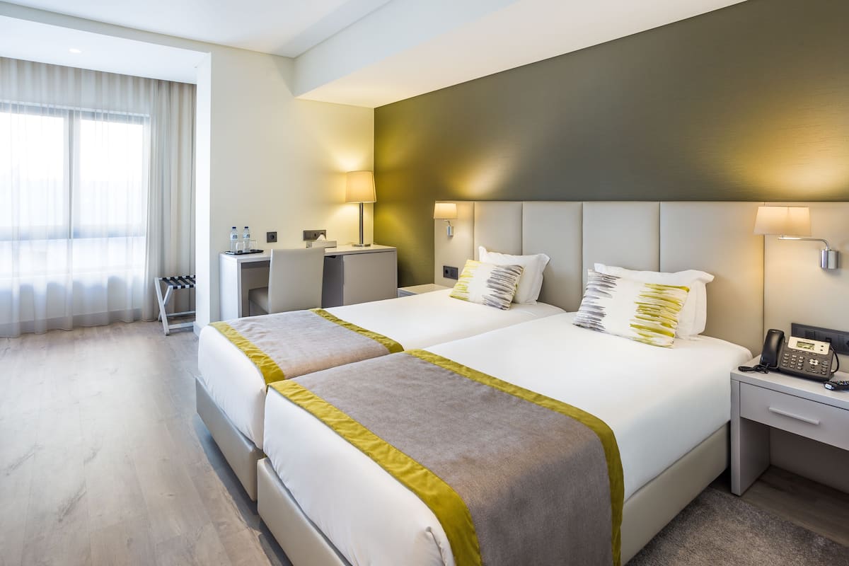 Een hotelkamer met twee bedden, een bureau, een stoel en een telefoon op het nachtkastje.