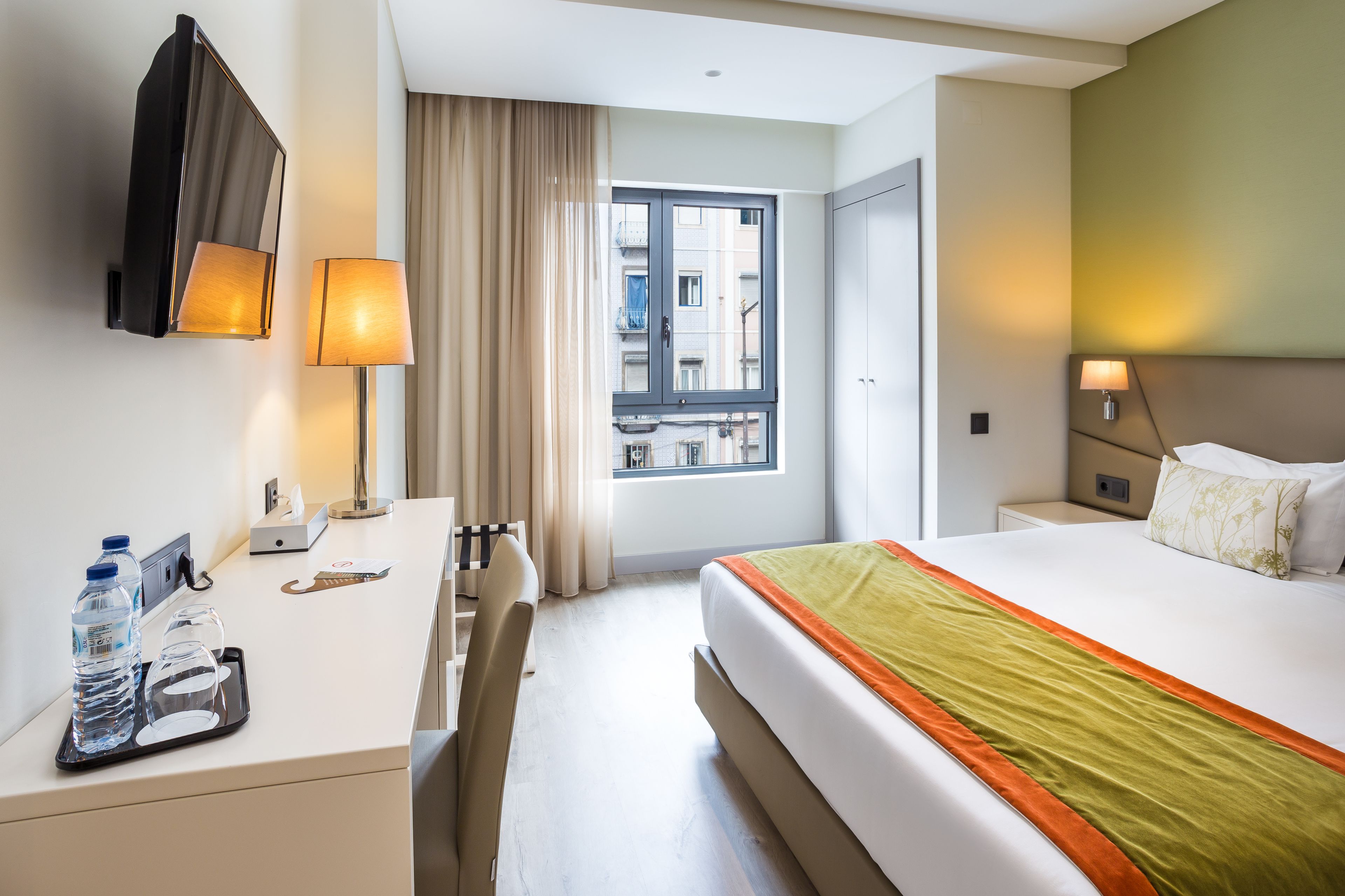 A hotel room with a bed, bedside table, lamp, and a window with curtains.