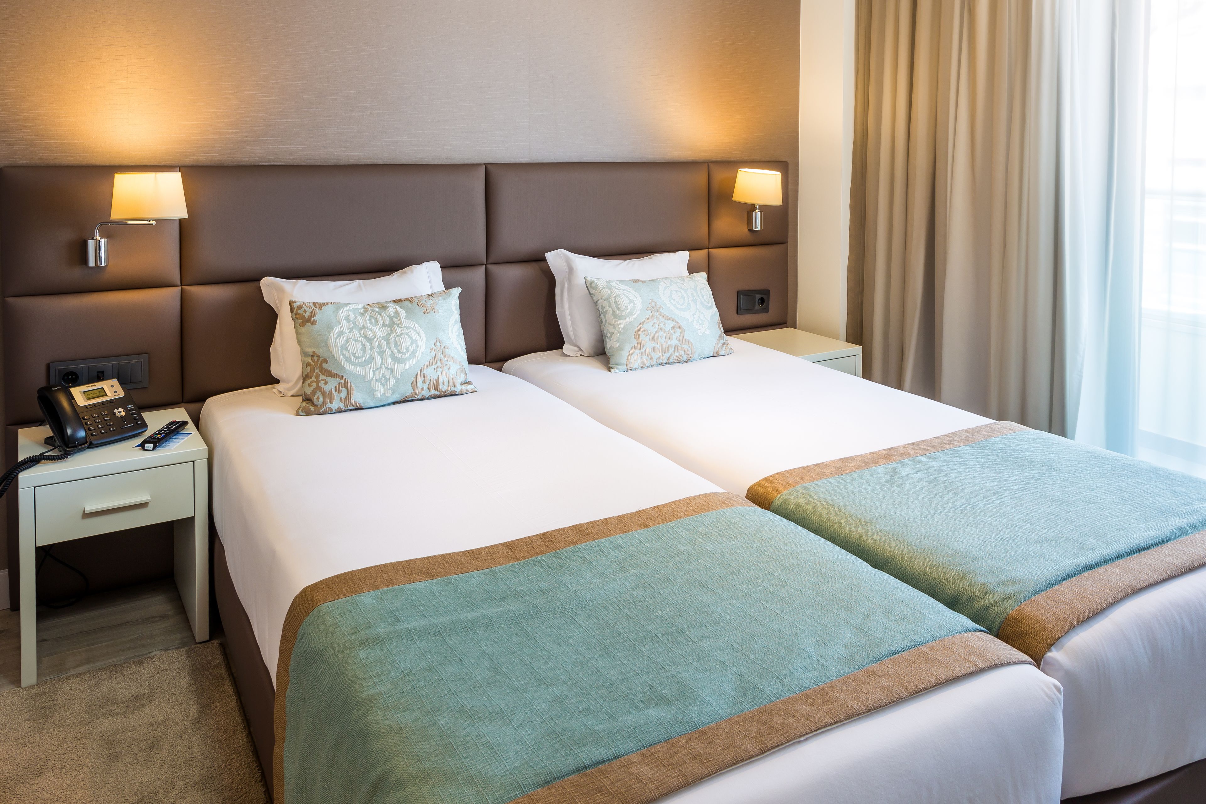A hotel room with two beds, a bedside table with a phone, and a lamp.