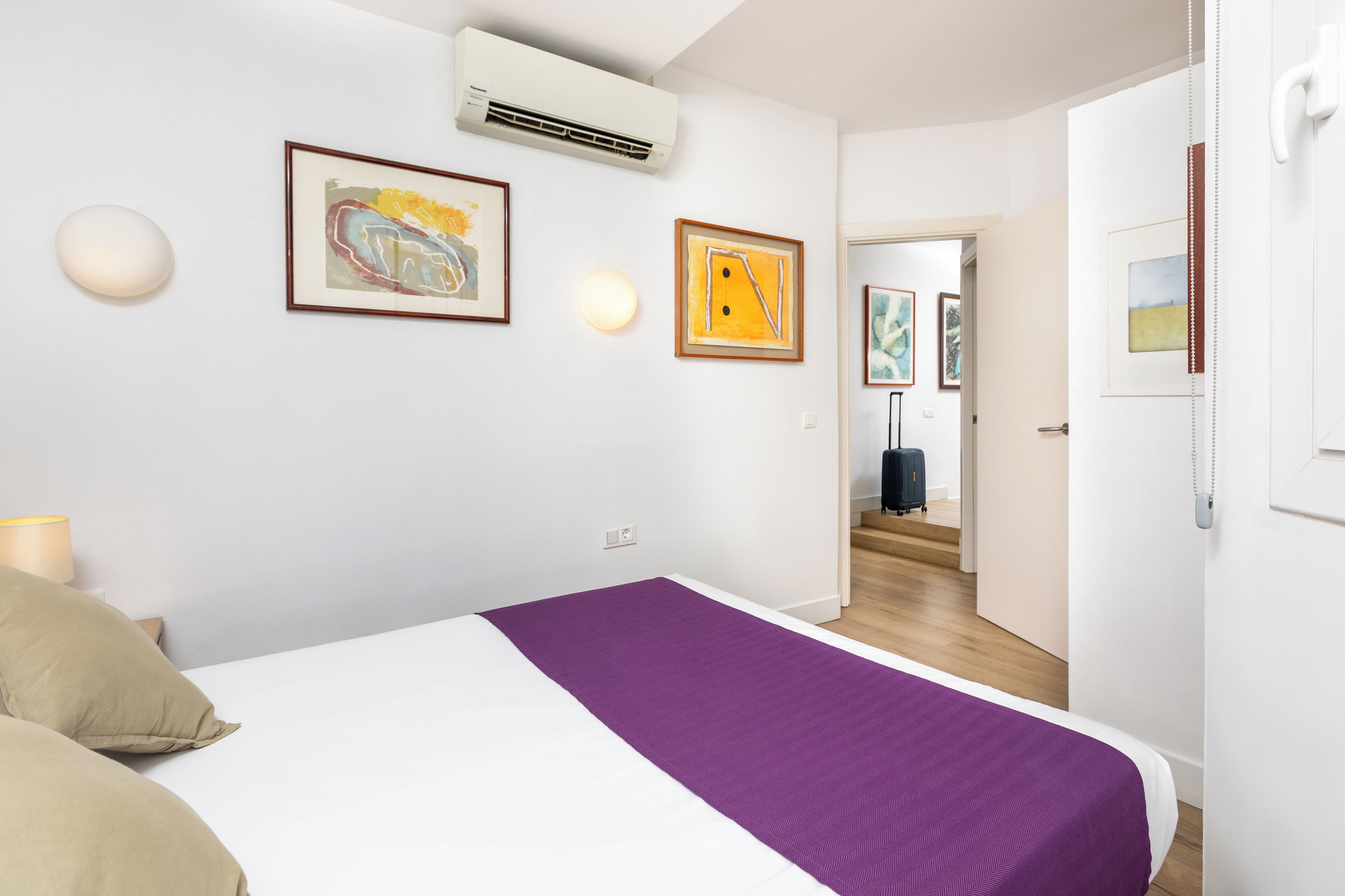 A modern hotel room with a bed, a purple bedspread, and artwork on the walls.