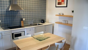 A modern kitchen with a built-in oven, microwave, and dishwasher. There is a wooden table with two chairs and a glass-top table. A sink with a faucet and a coffee maker are also visible. - Apartamentos Mayerling Bisbe Urquinaona (Barcelona)