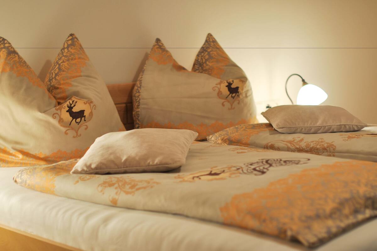 Een bed met beddengoed met een patroon en decoratieve kussens, inclusief een lamp op het nachtkastje.