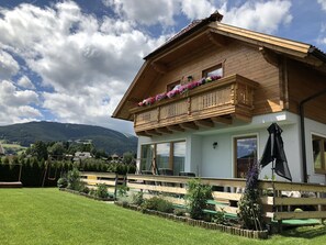A two-story wooden house with a balcony adorned with flowers, a wooden fence, and a grassy yard. - Sonnenchalets Mariapfarr (Mariapfarr)
