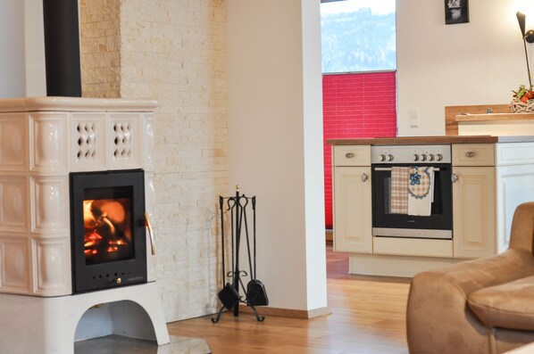A living room with a white fireplace, a kitchen with a stove, and a window with a red blind.
