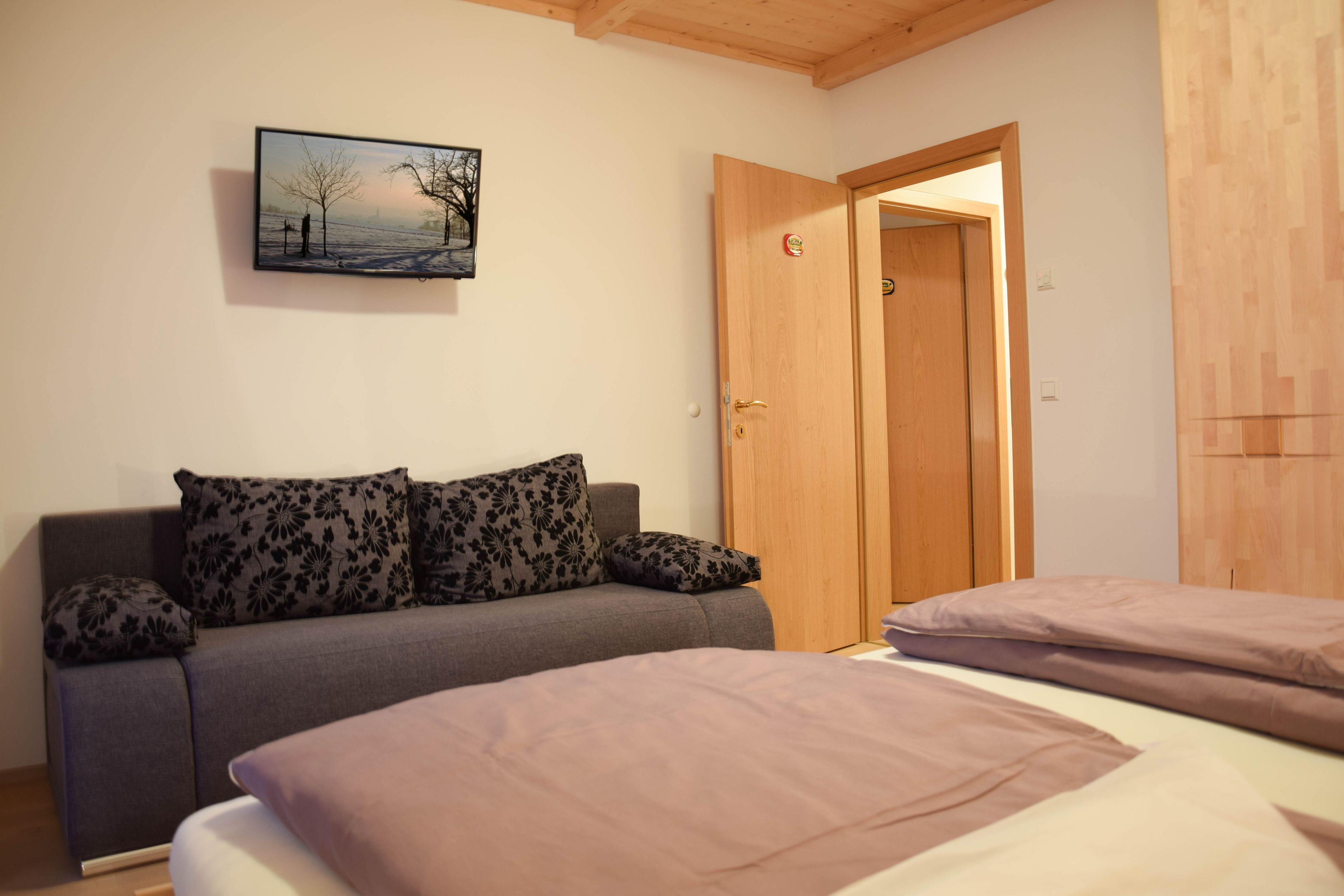 Una habitación con un sofá, dos camas, una puerta de madera y un cuadro en la pared.
