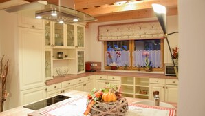 Une cuisine avec des meubles blancs, un pare-feu en verre et un îlot central agrémenté d’un panier tressé en guise de décoration.
