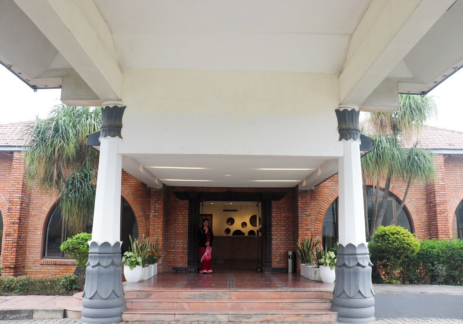 A building entrance with a covered porch, brick walls, and potted plants.