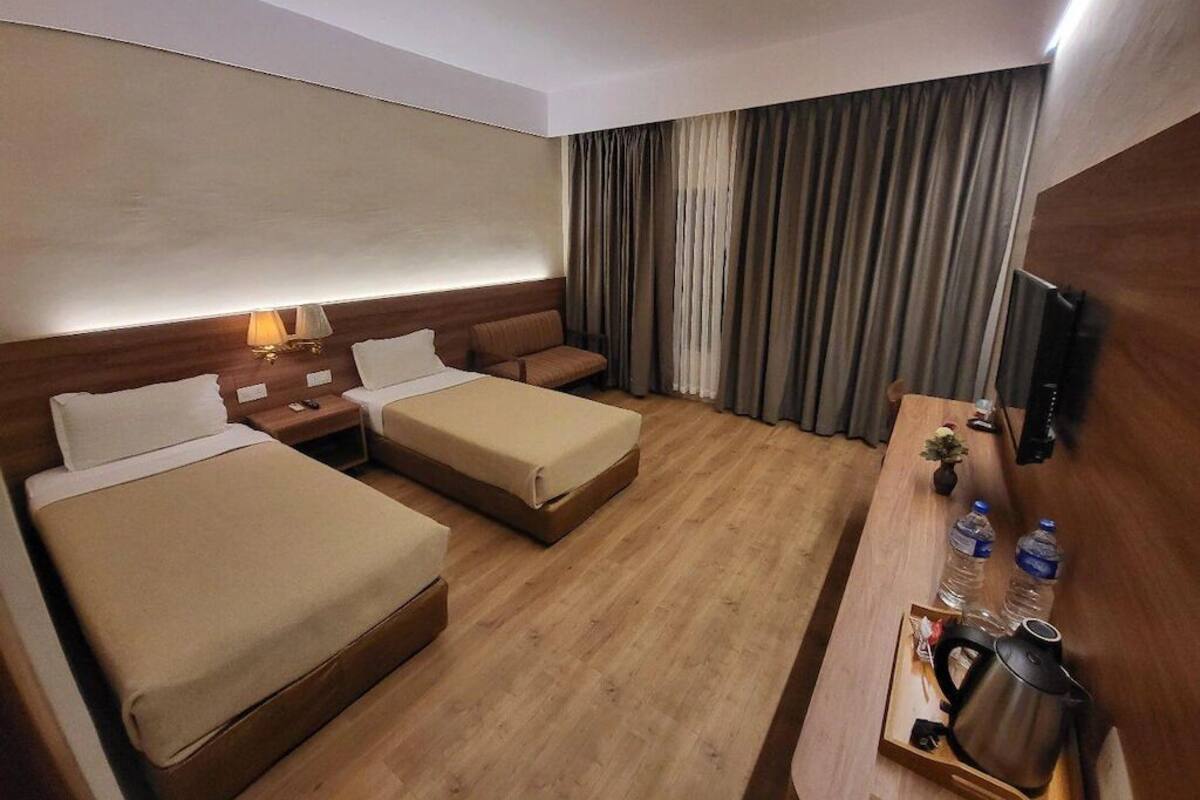 Une chambre d’hôtel avec deux lits, un bureau avec une bouilloire et une télévision.