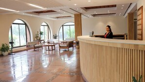 A reception area with a curved wooden reception desk, multiple seating arrangements, and large arched windows allowing natural light.
