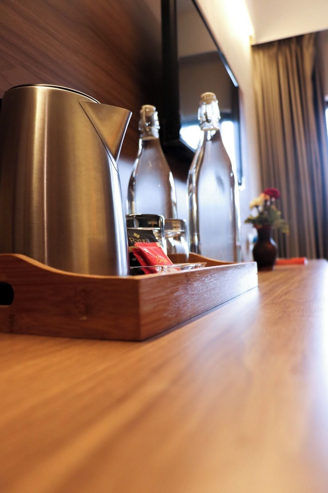 A wooden tray with a stainless steel kettle and two glass bottles on a wooden table.