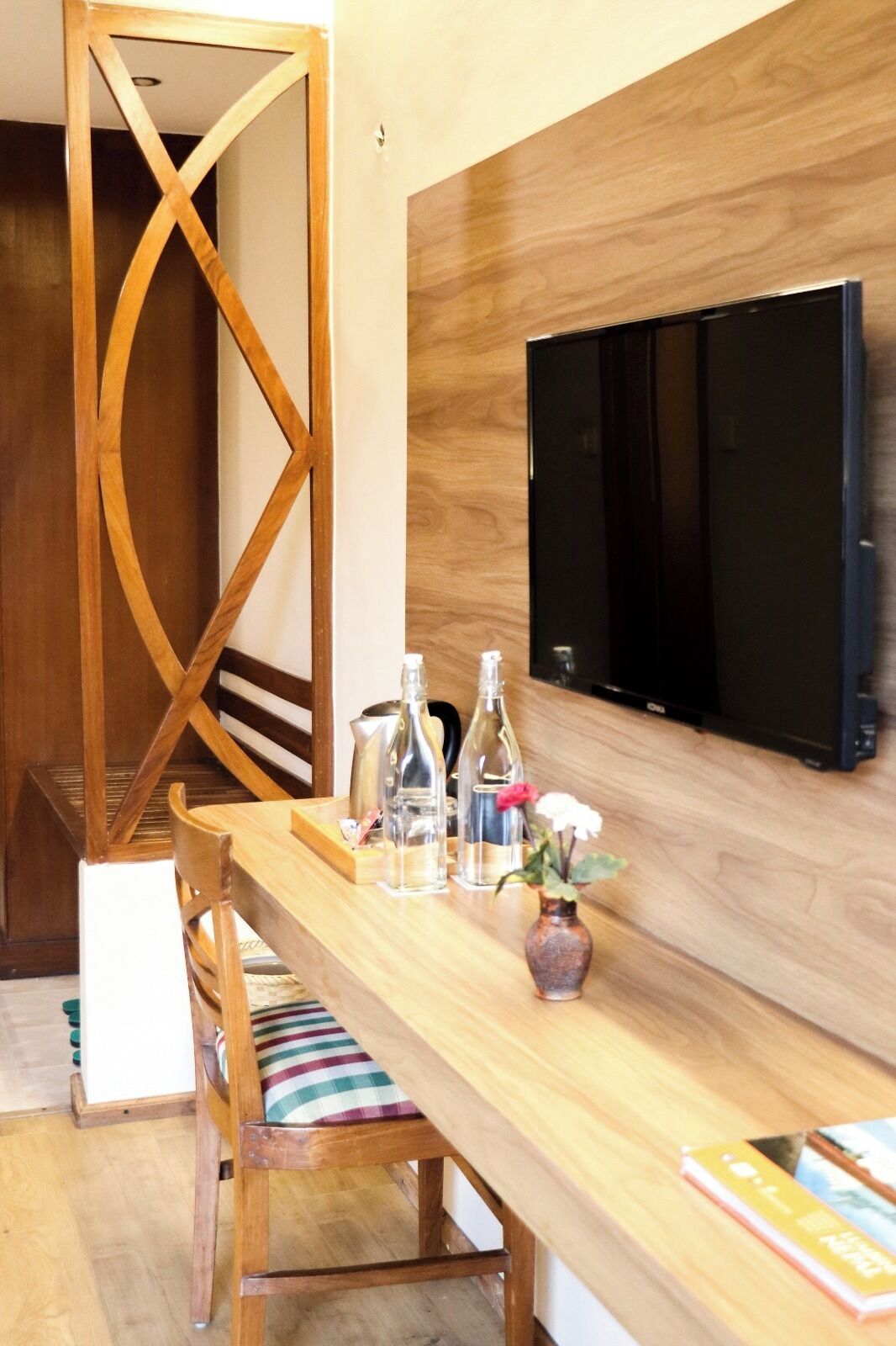 A wooden dining table with a TV mounted on the wall, a wooden chair with a striped cushion, and a vase with flowers.