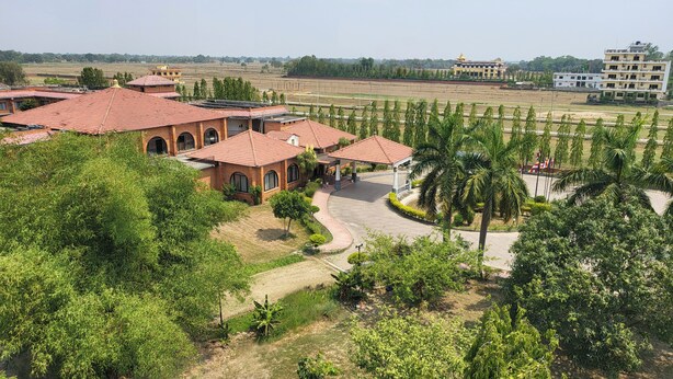 A large building with multiple red-roofed structures, surrounded by greenery and open fields.