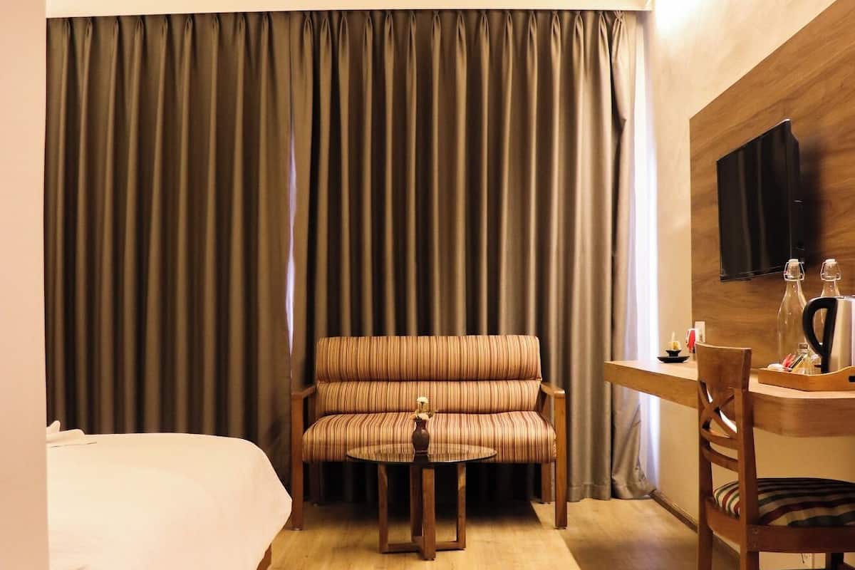 Une chambre d’hôtel avec un lit, un canapé, une petite table avec une chaise, un téléviseur fixé au mur et un rideau servant de décor.