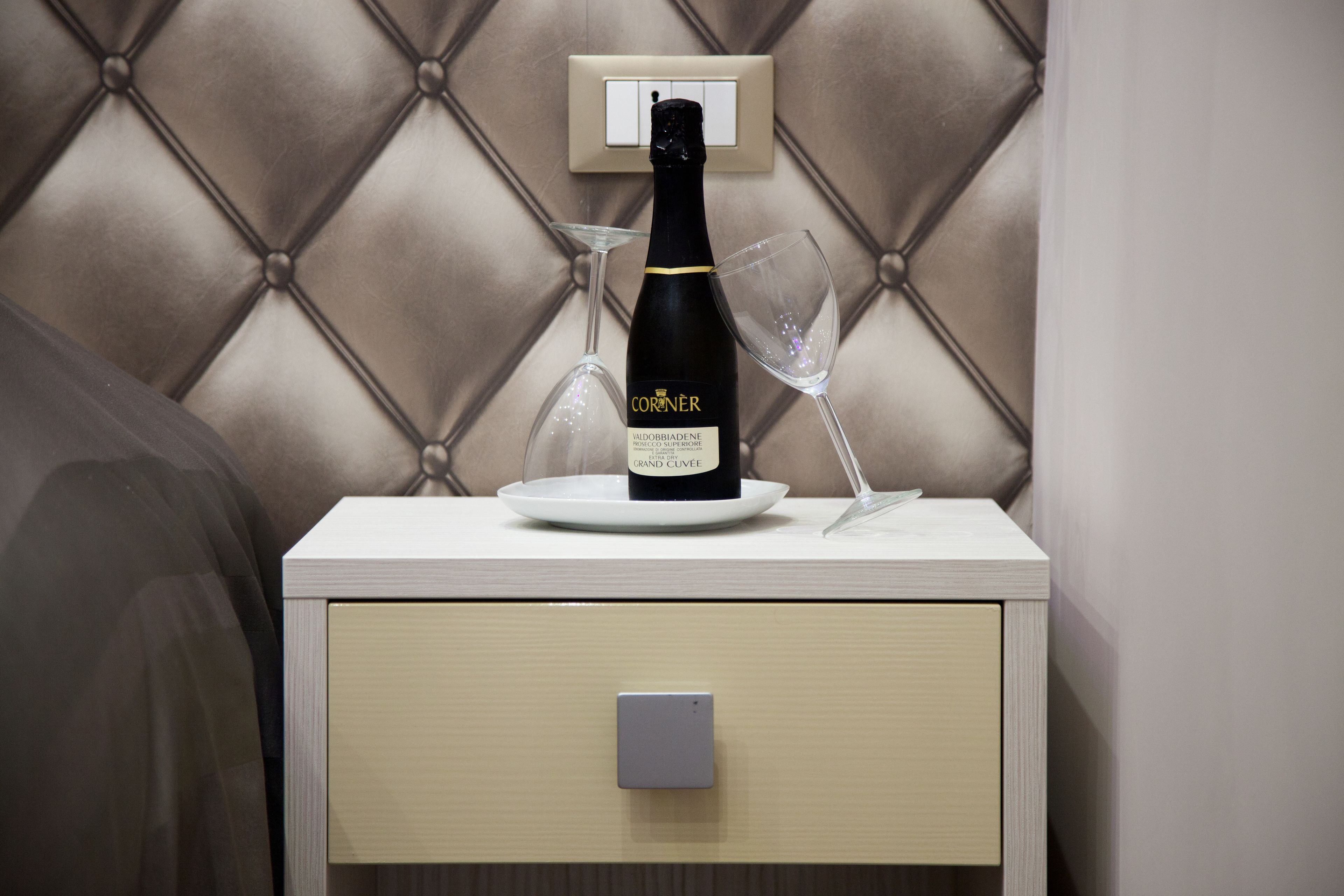A bottle of Corner Grand Cuvee on a bedside table with a glass and a charger.